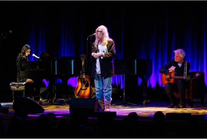 Patti Smith on stage with "Bread of Angels" memoir cover